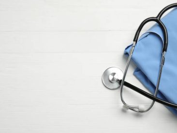 Stethoscope and medical uniform on white wooden background, flat lay. Space for text